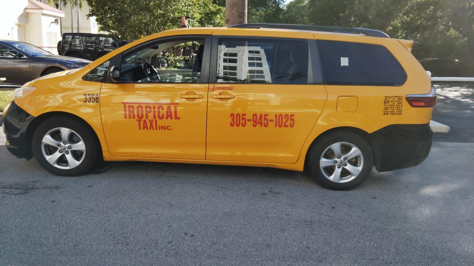 Yellow Tropical Taxi minivan parked on a street with trees and other cars in the background.