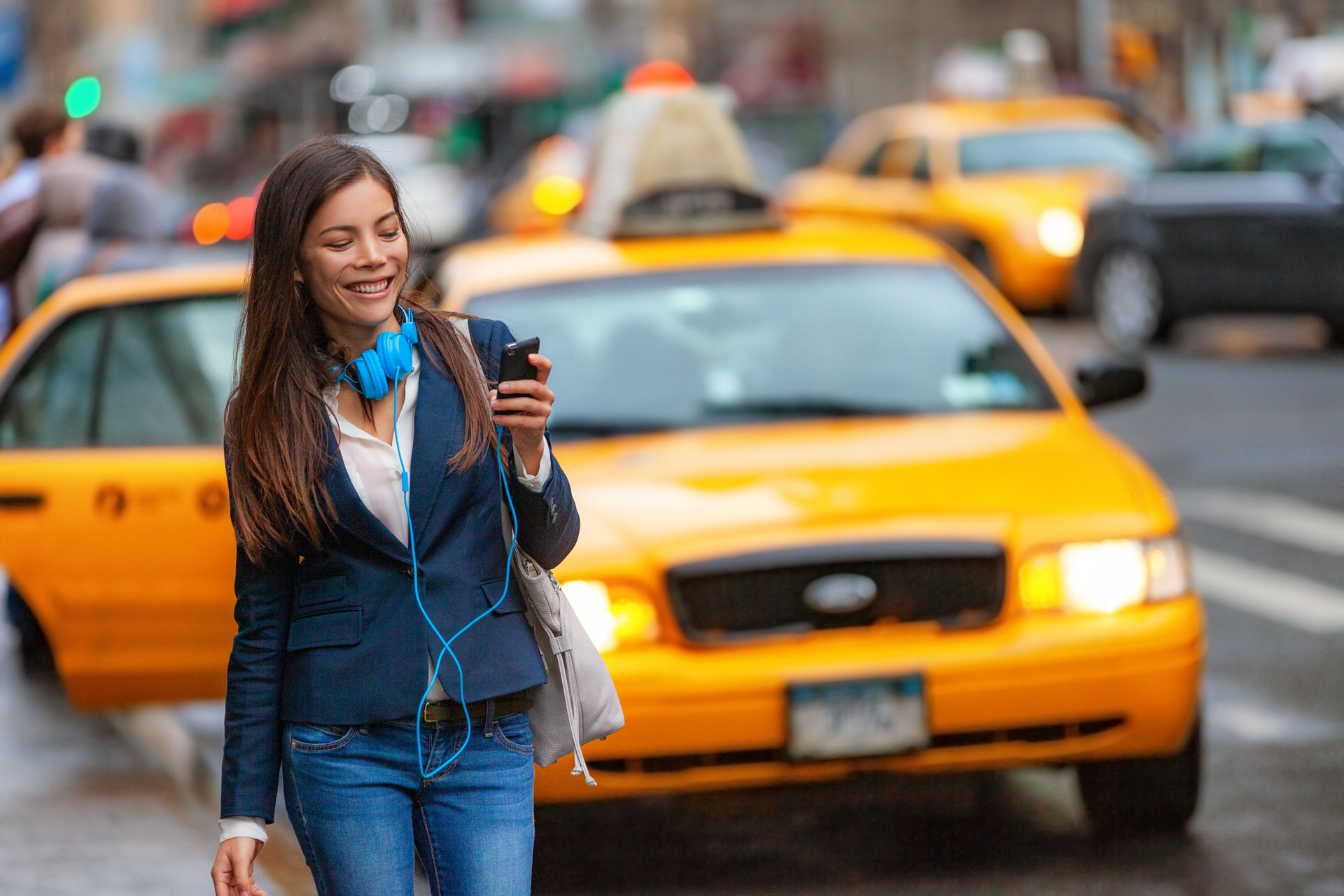 Young woman walking in New York city using phone app for taxi ride hailing with headphones commuting from work. Asian girl happy texting on smartphone. Urban walk commuter NYC