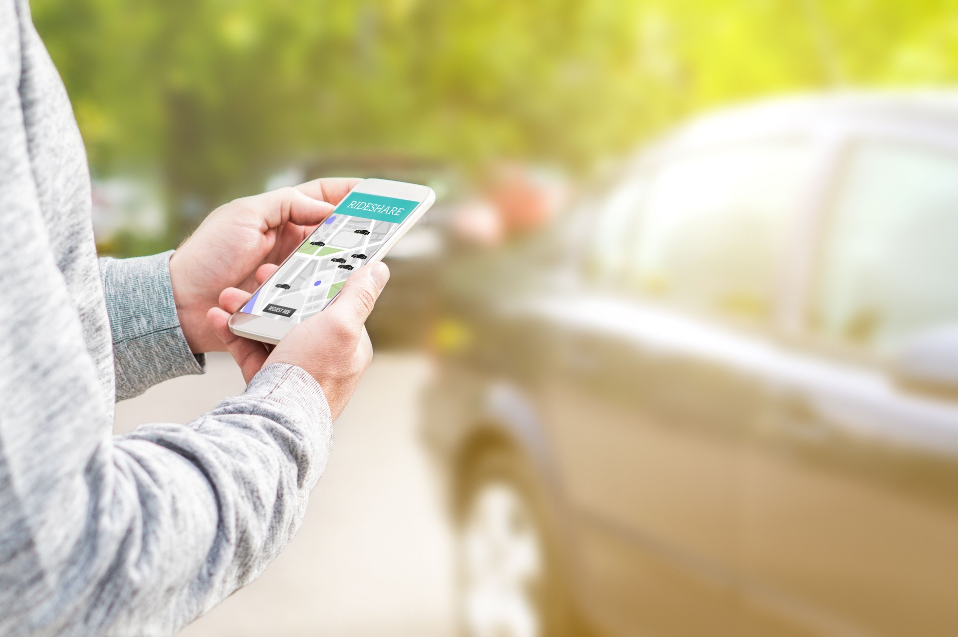 Online ride sharing and carpool mobile application. Rideshare taxi app on smartphone screen. Modern people and commuter transportation service. Man holding phone with a car in background.